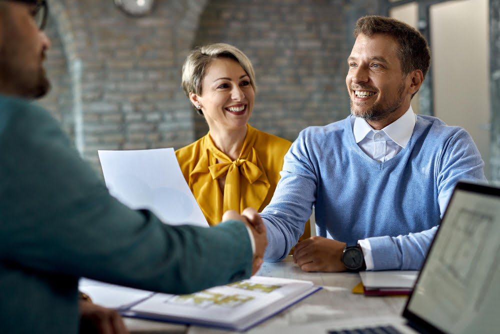 Como fazer portabilidade de empréstimo consignado? 2 happy couple shaking hands with real estate agent after successful agreement office