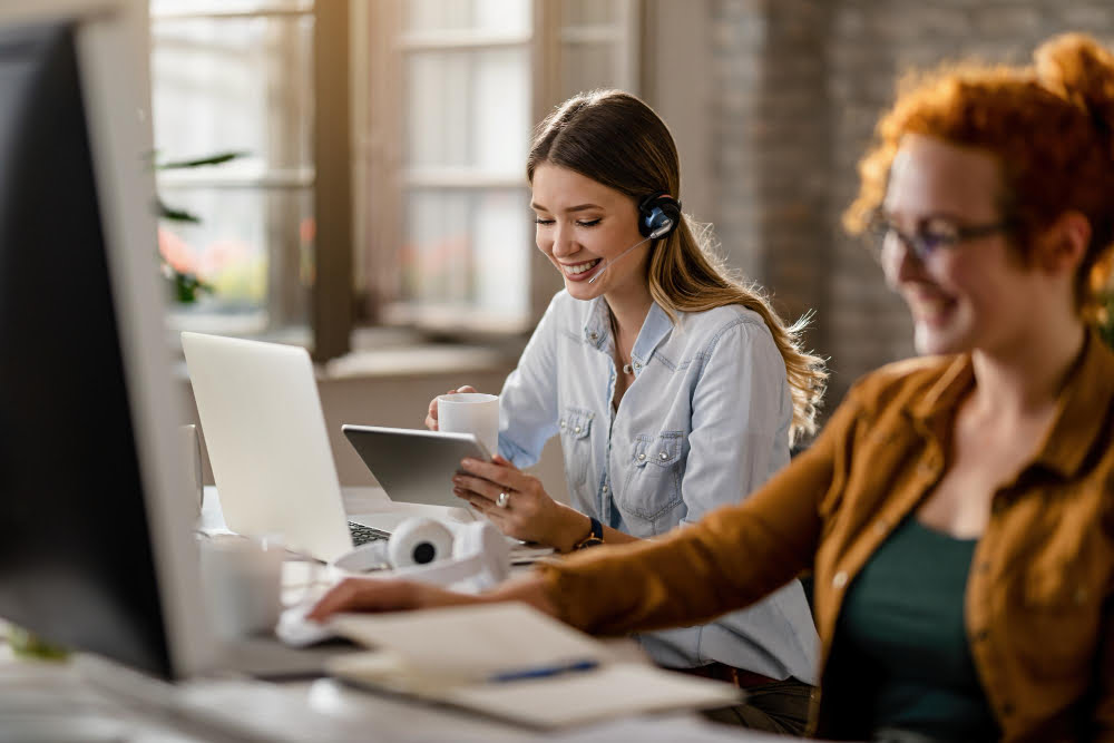 Qual operadora de celular faz atendimento via WhatsApp? 4 happy female entrepreneur with headset drinking coffee while surfing the net on touchpad in the office