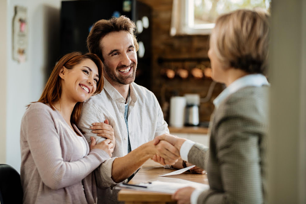 Como fazer portabilidade de empréstimo consignado? 4 young happy couple came agreement with their insurance agent focus is man shaking hands with agent