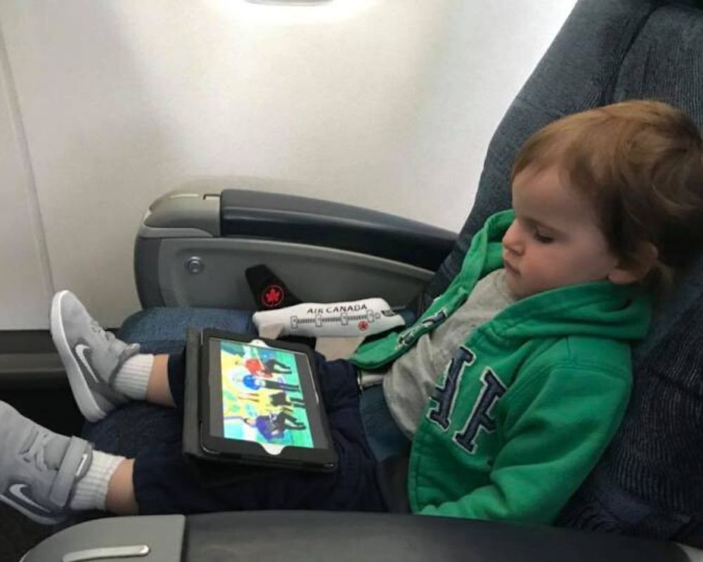 Dicas sobre como viajar com crianças pequenas 2 Garoto no avião mantendo-se calmo, quieto e assistindo a um ipad