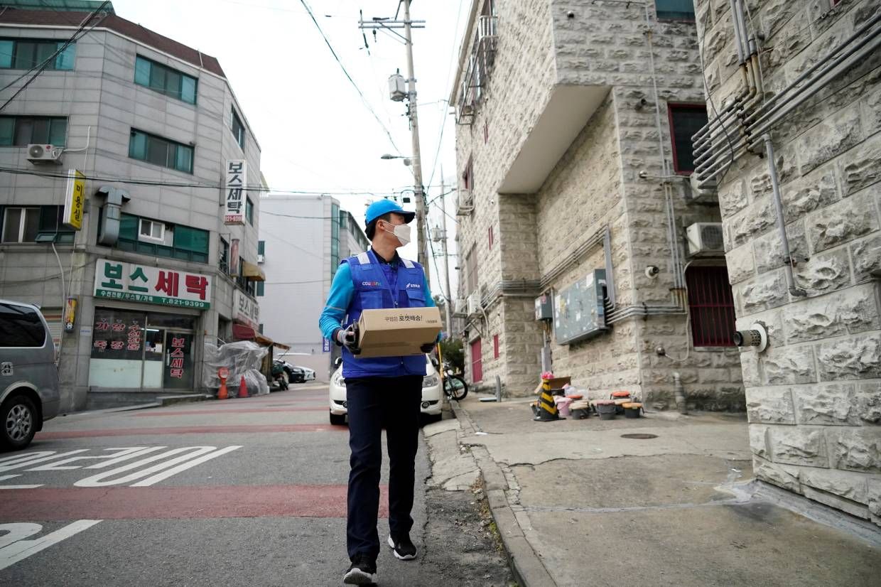 um entregador de encomendas de azul usando uma máscara protetora entrega uma caixa