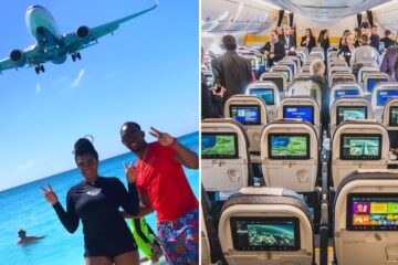 two people throw up the peace sign as a plane flies overhead, on board a caymen airways plane