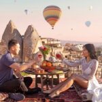 a couple has dinner at sunset while watching hot air balloons in Cappadocia, Turkey