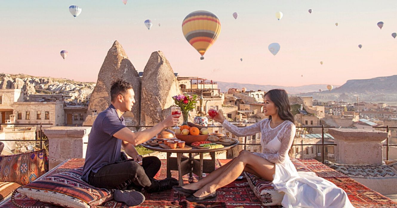 um casal janta ao pôr do sol enquanto assiste a balões de ar quente na Capadócia, Turquia