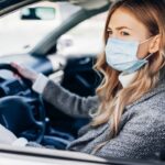 uma mulher dirigindo um carro com uma máscara facial