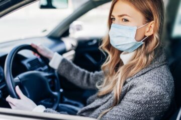 uma mulher dirigindo um carro com uma máscara facial