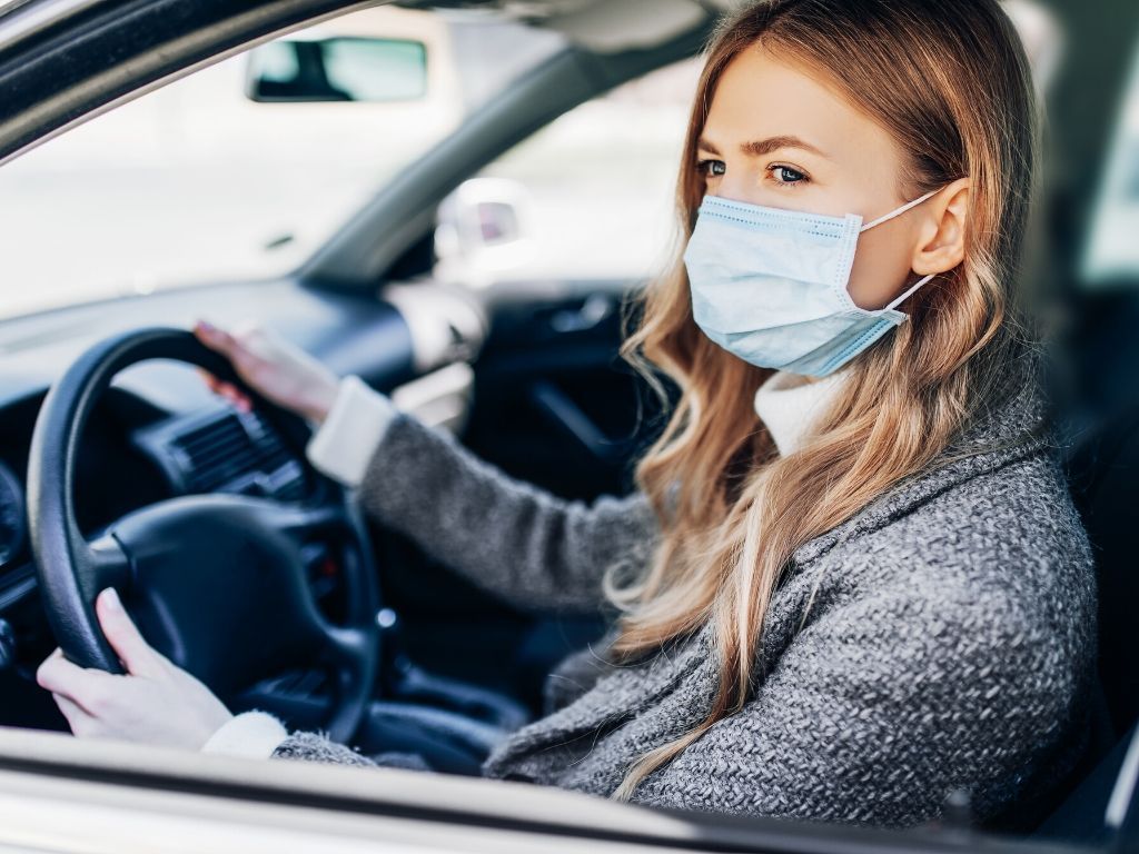 Os aluguéis por temporada estão disparando, e isso é o que você deve fazer antes de reservar 1 uma mulher dirigindo um carro com uma máscara facial
