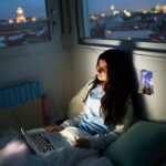 a girl sits on her laptop at night in the city
